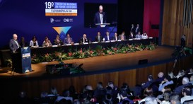 #PraTodosVerem: Na fotografia aparece um auditório em um evento formal, onde um homem de terno e...