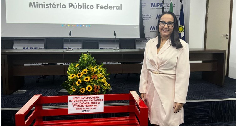 #PraTodosVerem: Na fotografia aparece uma mulher ao lado de um banco vermelho e por trás um arra...
