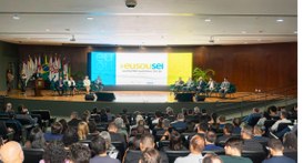 #PraTodosVerem: Na fotografia aparece um auditório com pessoas sentadas de costas pra imagem e d...