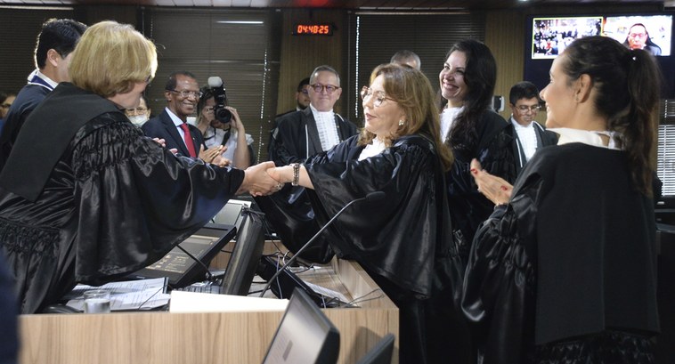 TRE-PB posse da desembargadora Agamenilde Dias Pessoas de pé e ao centro, duas mulheres se cumprimentam com aperto de mãos.