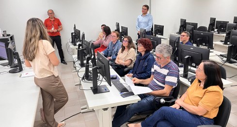 #PraTodosVerem: Na fotografia, um grupo de pessoas está reunido em uma sala de treinamento, sorr...