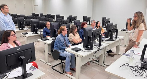 #PraTodosVerem: Na fotografia, um grupo de pessoas está reunido em uma sala de treinamento, sorr...