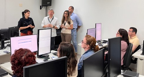 #PraTodosVerem: Na fotografia, um grupo de pessoas está reunido em uma sala de treinamento, sorr...