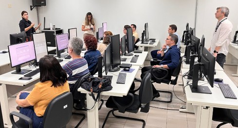 #PraTodosVerem: Na fotografia, um grupo de pessoas está reunido em uma sala de treinamento, sorr...