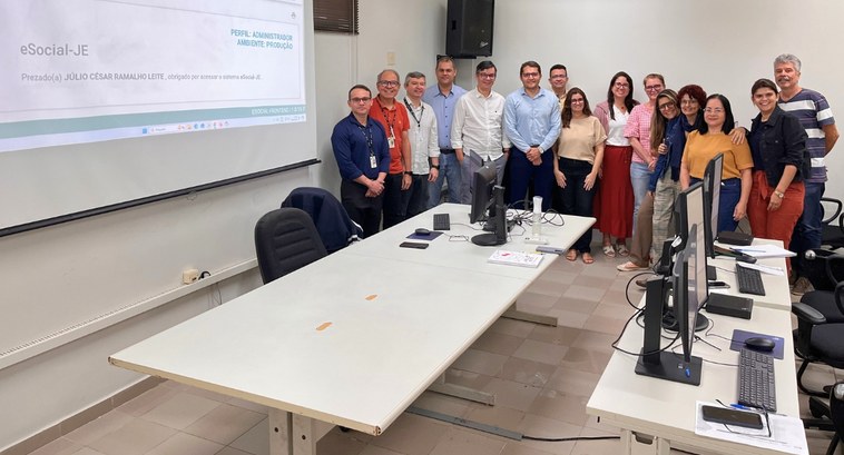 #PraTodosVerem: Na fotografia, um grupo de pessoas está reunido em uma sala de treinamento, sorr...