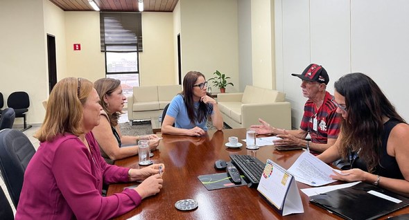 #PraTodosVerem: Na fotografia interna aparecem pessoas sentadas em uma sala de reunião. 