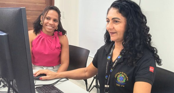 #PraTodosVerem: Na fotografia aparece uma servidora do TRE-PB atendendo uma jovem. A servidora e...