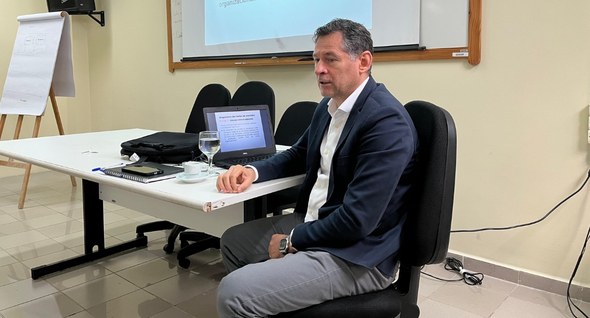 TRE-PB realiza Oficina sobre Inventário de Gases de Efeito Estufa #PraTodosVerem: Na fotografia, aparece um homem em primeiro plano. Ele está sentado em uma cadei...