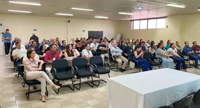#PraTodosVerem: Na fotografia aparece um auditório, com paredes claras, onde cerca de 50 pessoas...