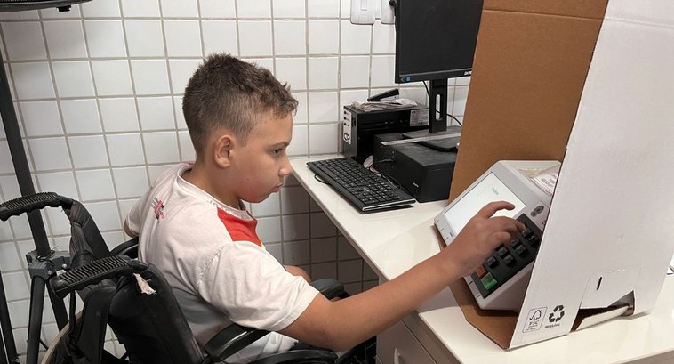 #PraTodosVerem: Na fotografia aparece uma criança com deficiência física votando na urna eletrôn...