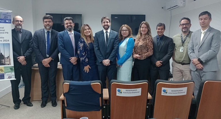 Painel retangular com dez pessoas perfiladas, posando para fotografia, três são mulheres.
