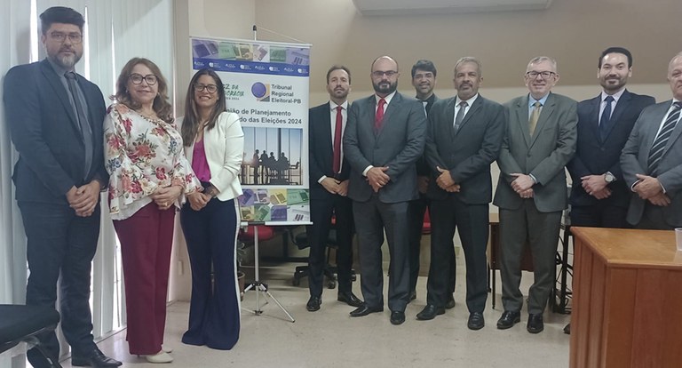 Painel retangular com dez pessoas perfiladas, posando para fotografia, duas são mulheres.