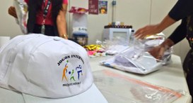 #PraTodosVerem: Na fotografia aparece um boné em uma mesa em primeiro plano com a logomarca dos ...