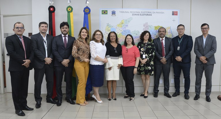 Painel retangular com onze pessoas, das quais cinco mulheres, perfiladas, posando para fotografia.