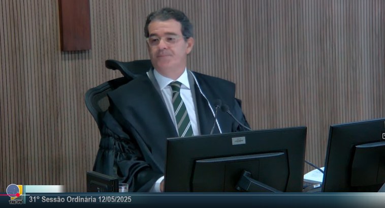 TRE-PB voto aplauso para Renato César #PraTodosVerem: um homem sentado à mesa com dois monitores de computador a sua frente, ele olha ...