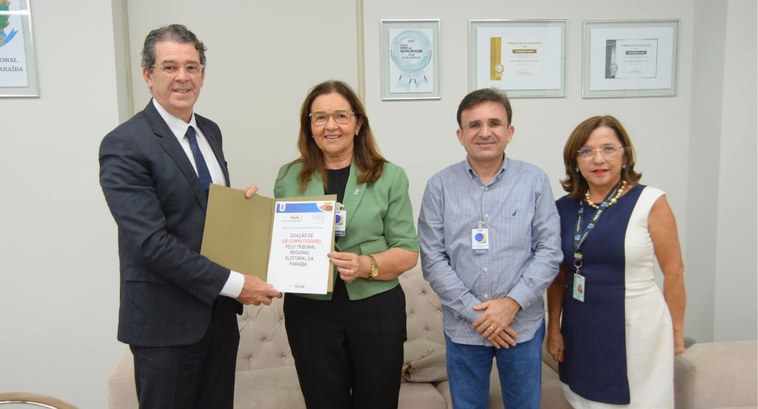 tre-pb_Doações UFPB - foto capa #PraTodosVerem: Na fotografia aparecem quatro pessoas posam sorridentes em um escritório. Uma mu...