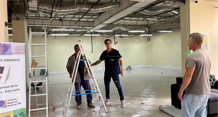 #PraTodosVerem: Na fotografia aparece uma sala em obras tendo duas escadas abertas e três pessoa...
