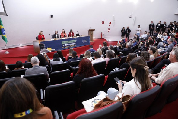 #PraTodosVerem: Na fotografia aparece um auditório, com pessoas, de costas, sentadas em poltrona...