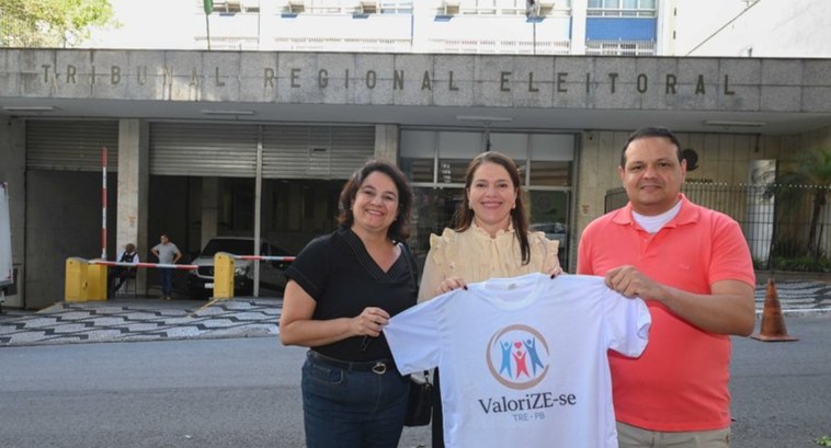 #PraTodosVerem: Na fotografia aparece um grupo de três pessoas, sendo duas mulheres e um homem, ...