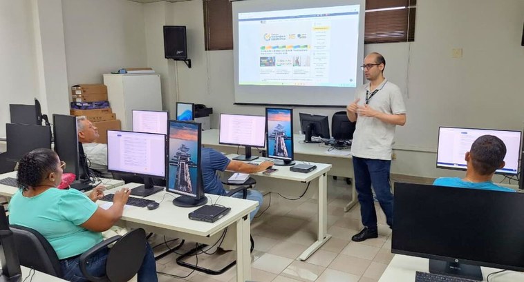 #PraTodosVerem: Na fotografia aparece uma sala de treinamento com pessoas sentadas em frente a t...