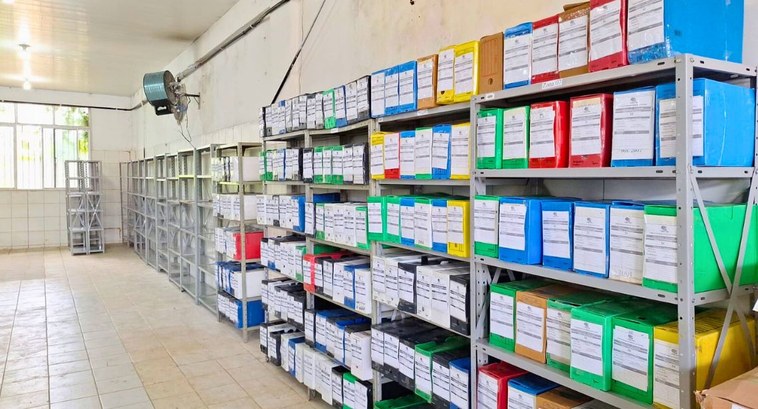 TRE-PB começa transferência de documentos dos cartórios para arquivo único #PraTodosVerem: Na fotografia de capa aparecem estantes arrumadas numa parede de uma sala com pr...