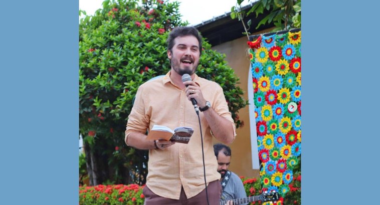 TRE-PB sedia exposição “Alma-de-Gato no Voo da Alvorada” #PraTodosVerem: Na fotografia aparece um homem, em pé, segurando um microfone em uma das mãos, e...